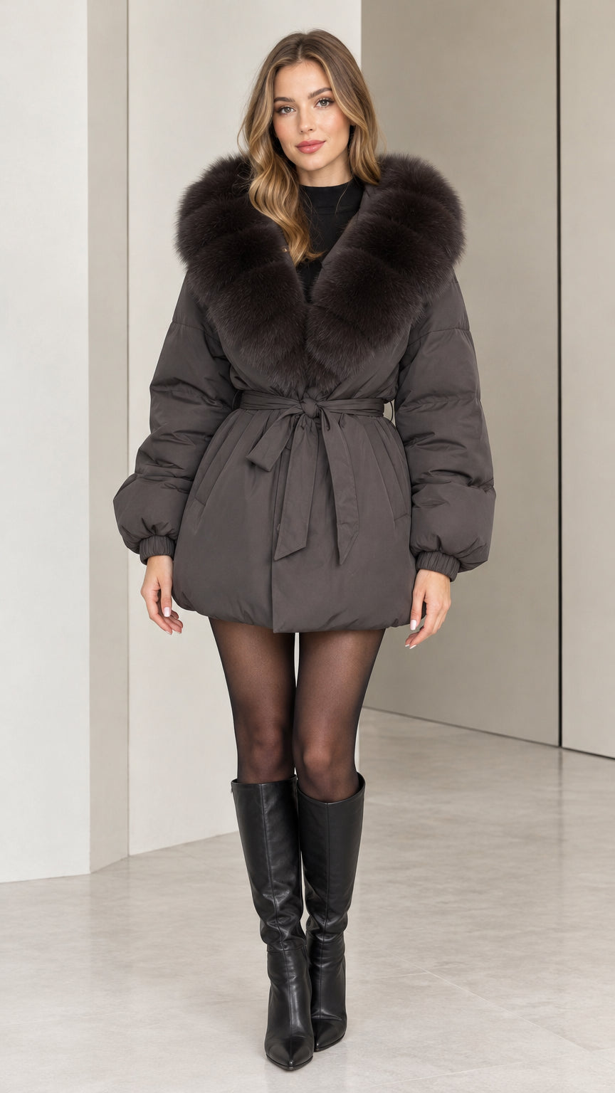 Front full-length view of woman wearing dark grey belted puffer coat with faux fur collar and knee boots