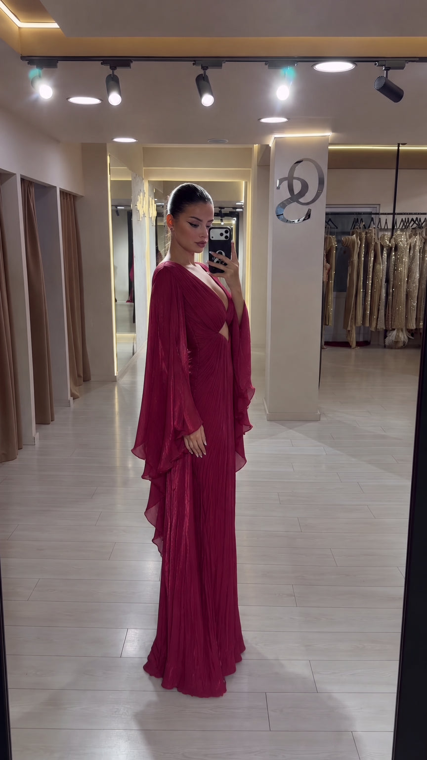 Side mirror selfie showing the drape and silhouette of the burgundy pleated maxi gown