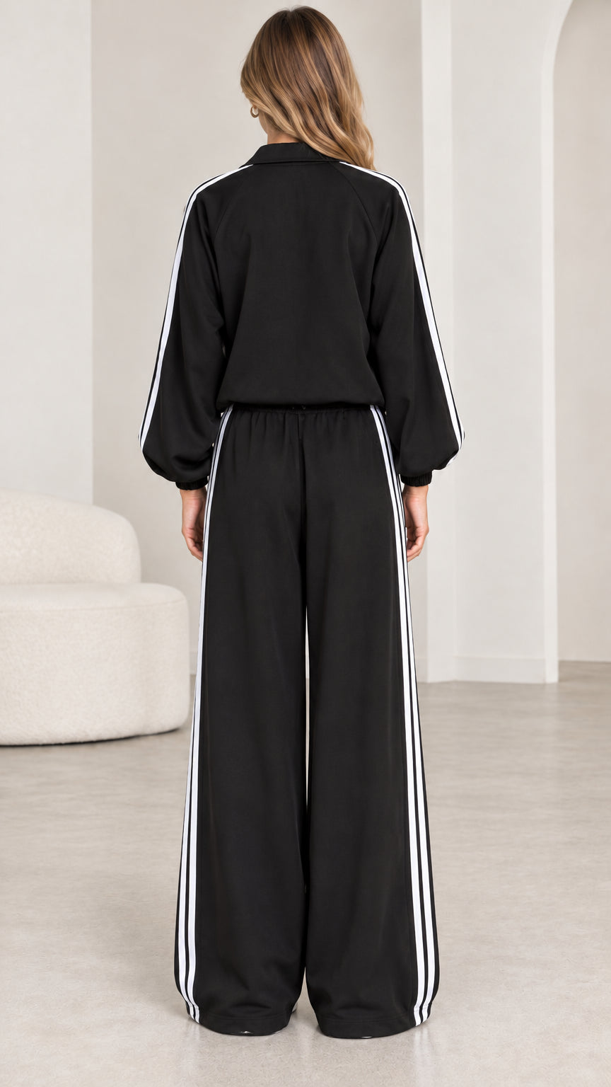 Back view of model in black tracksuit showing relaxed fit and side stripe pants
