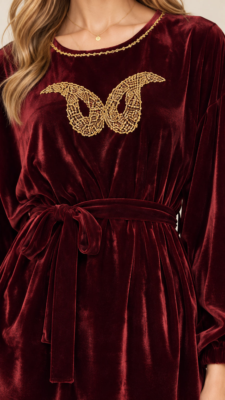 Close-up detail of golden butterfly embellishment and neckline on burgundy velvet top