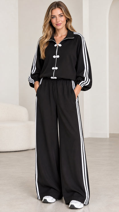Full front view of model wearing black zip-up tracksuit set with frog buttons and side stripes