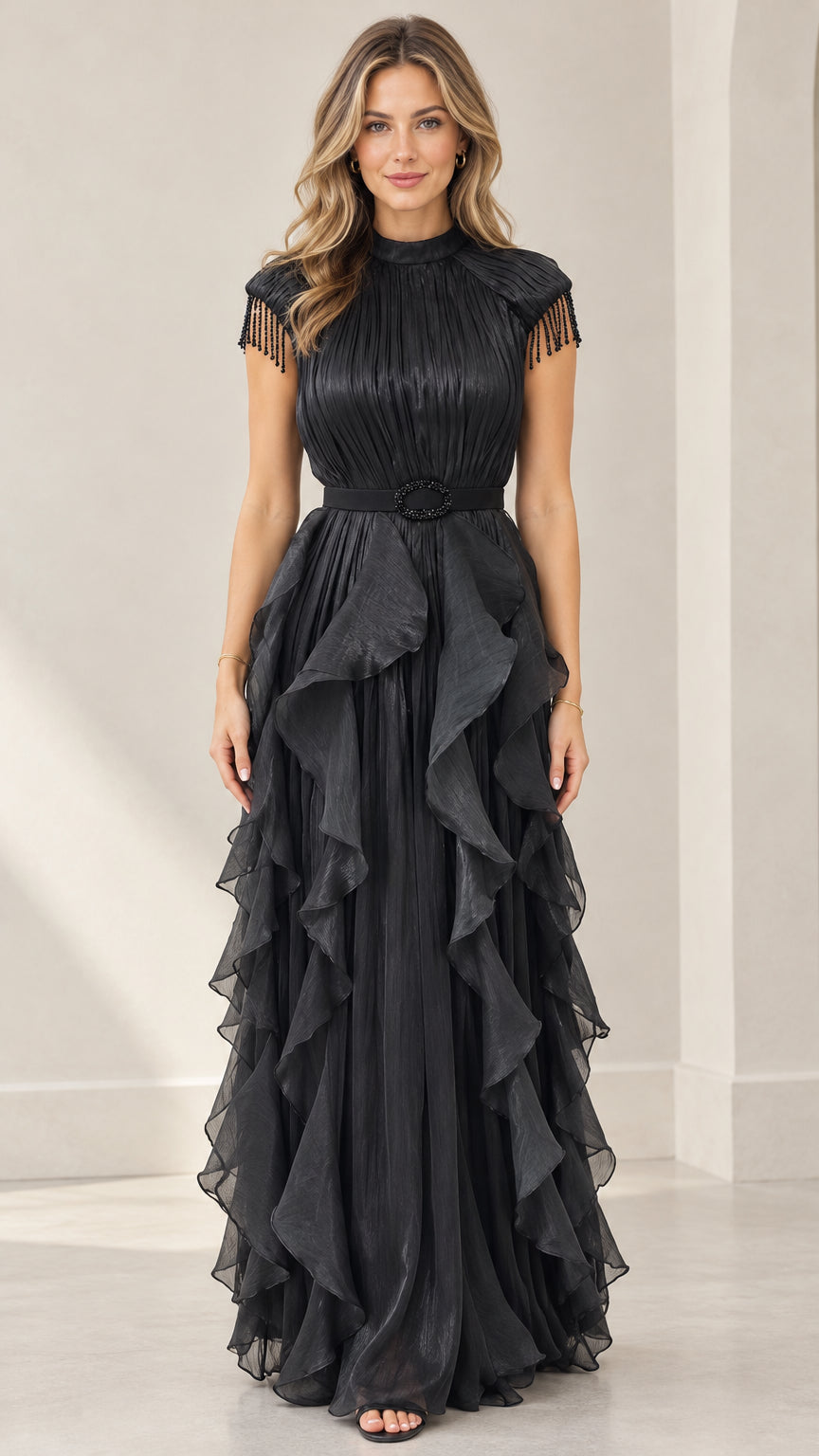 Front full-length view of woman wearing black pleated tiered ruffle evening maxi dress with beaded fringe cap sleeves