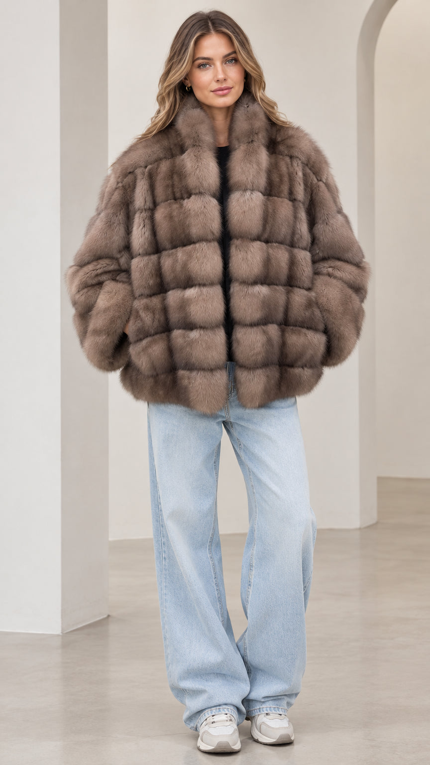 Front view of model wearing a taupe paneled faux fur jacket with light wash jeans