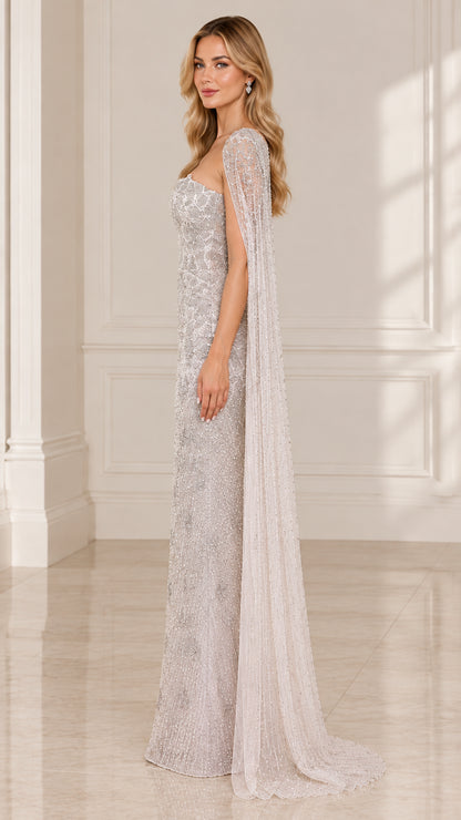 Side profile view of silver embellished strapless formal gown with flowing cape