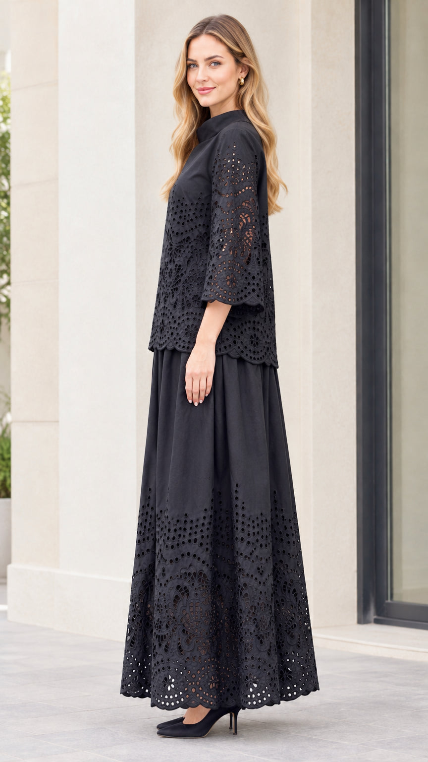 Side full-length view of woman in black two-piece embroidered blouse and pleated maxi skirt