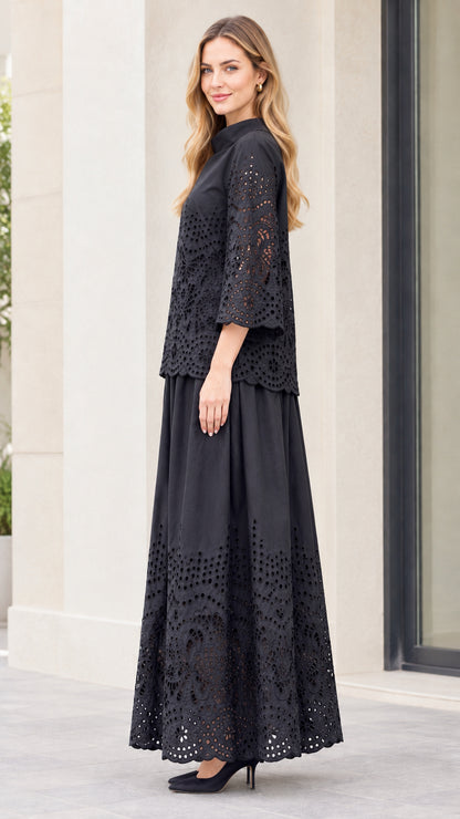 Side full-length view of woman in black two-piece embroidered blouse and pleated maxi skirt