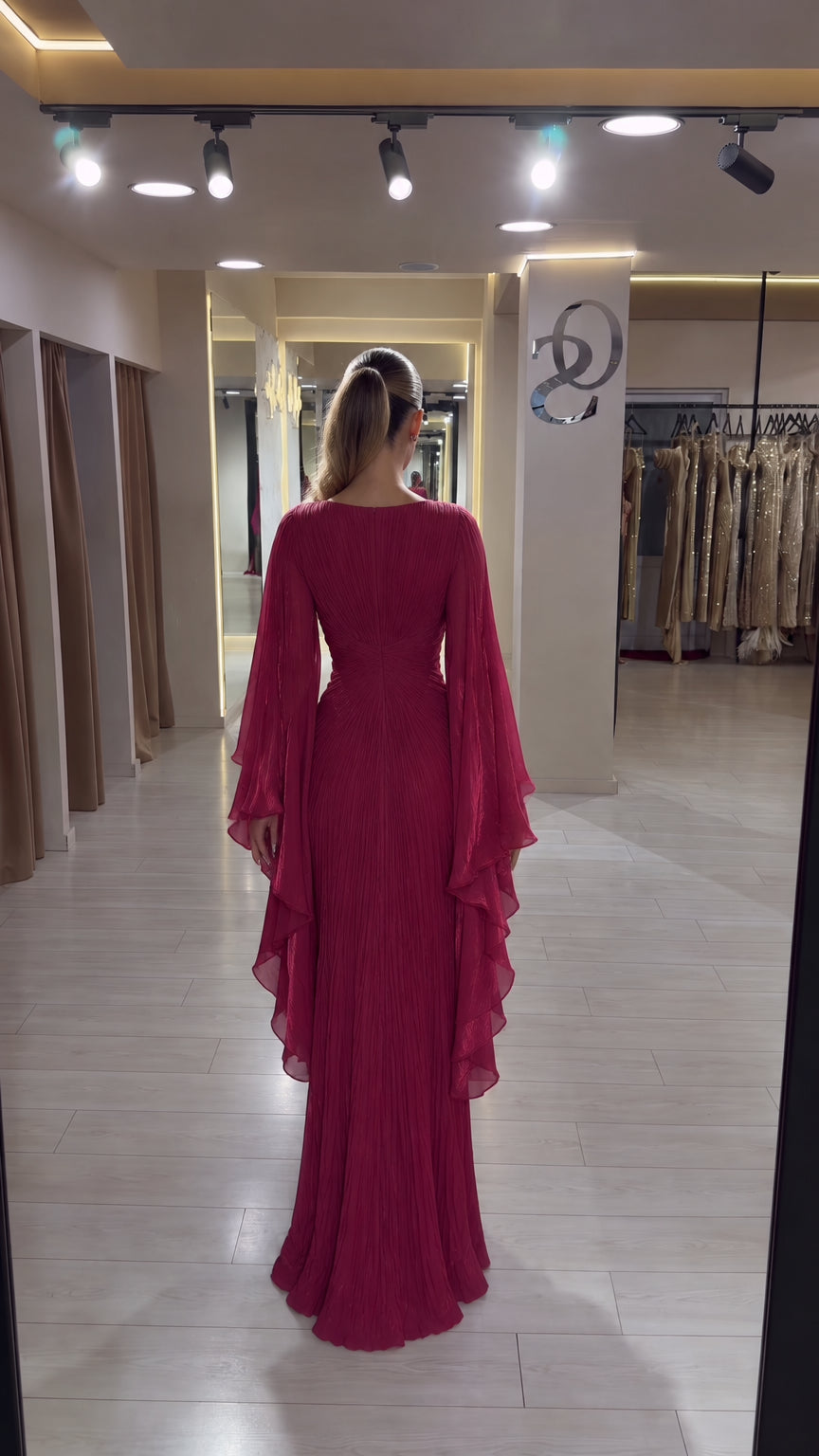 Back view of model showing the full-length pleated skirt and draped sleeves in burgundy