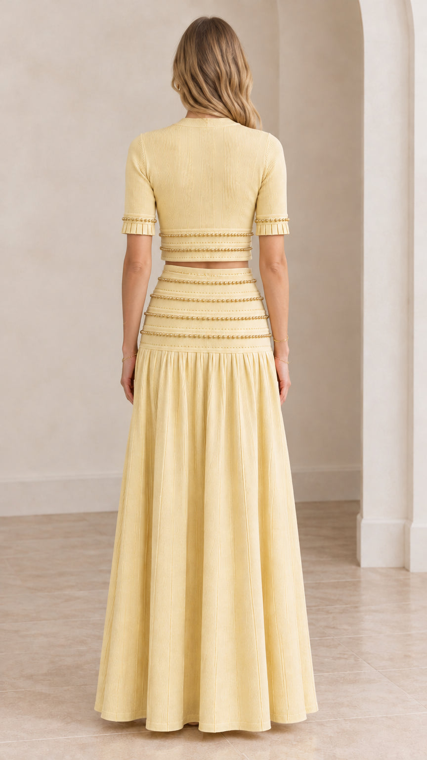 Back view of model in butter yellow two-piece crop top and pleated maxi skirt