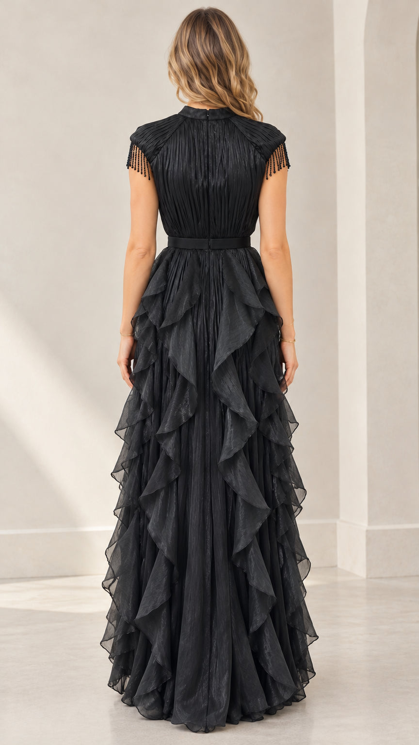 Back full-length view of woman in black mock neck pleated evening dress with layered ruffles