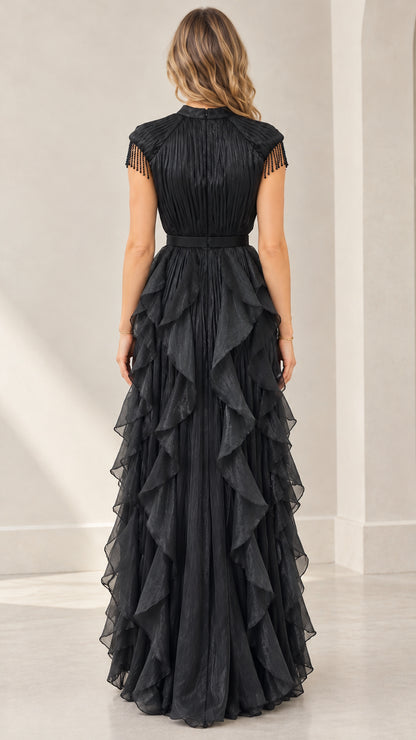 Back full-length view of woman in black mock neck pleated evening dress with layered ruffles