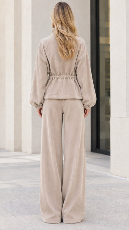Back view of model wearing beige ribbed zip jacket with drawstring waist and wide pants