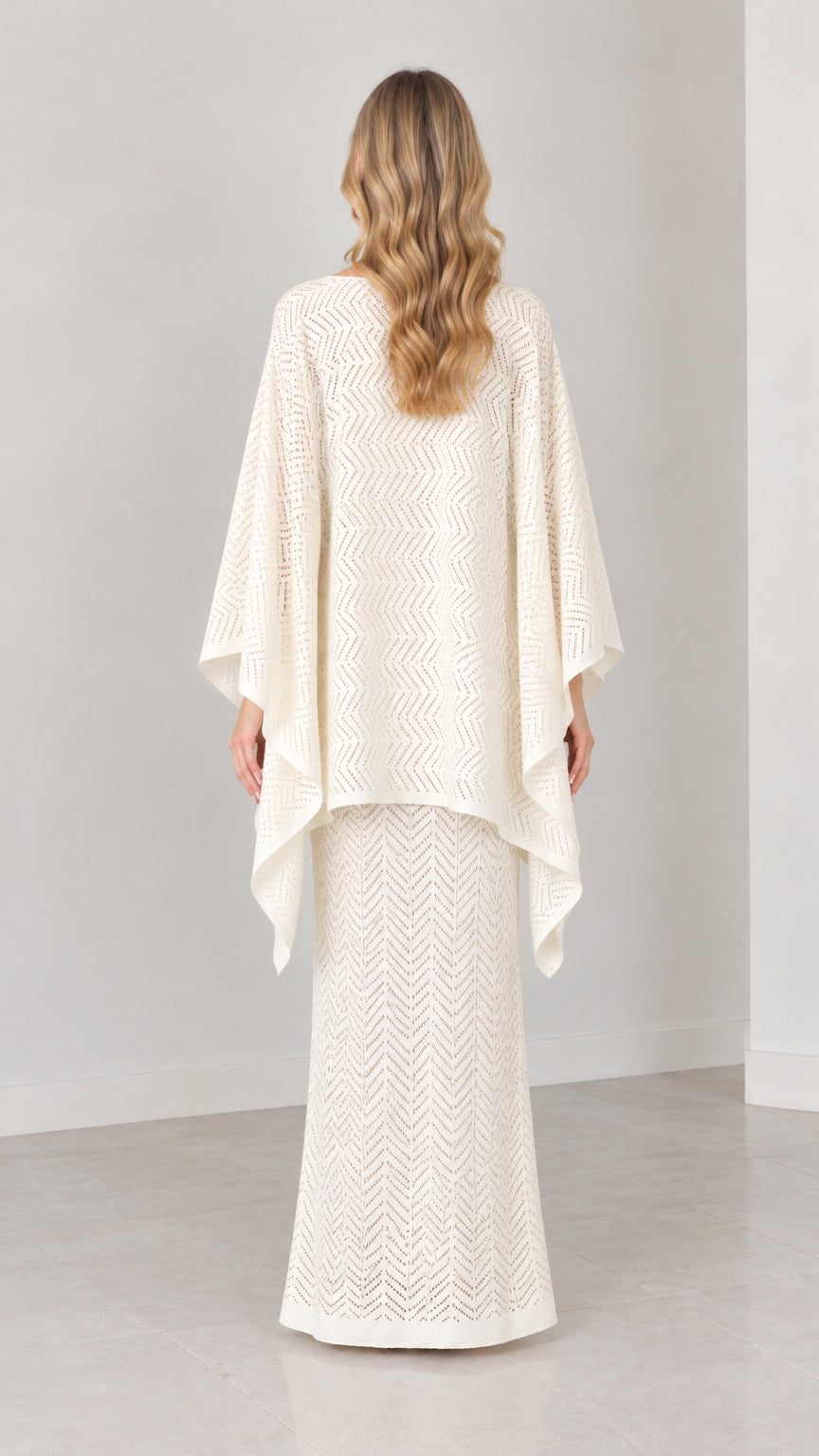 Back view of model wearing cream draped cape knit two-piece set