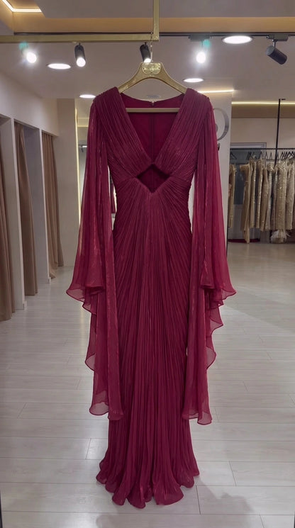 Burgundy pleated formal gown on hanger highlighting the V-neckline, cutout, and long cape sleeves