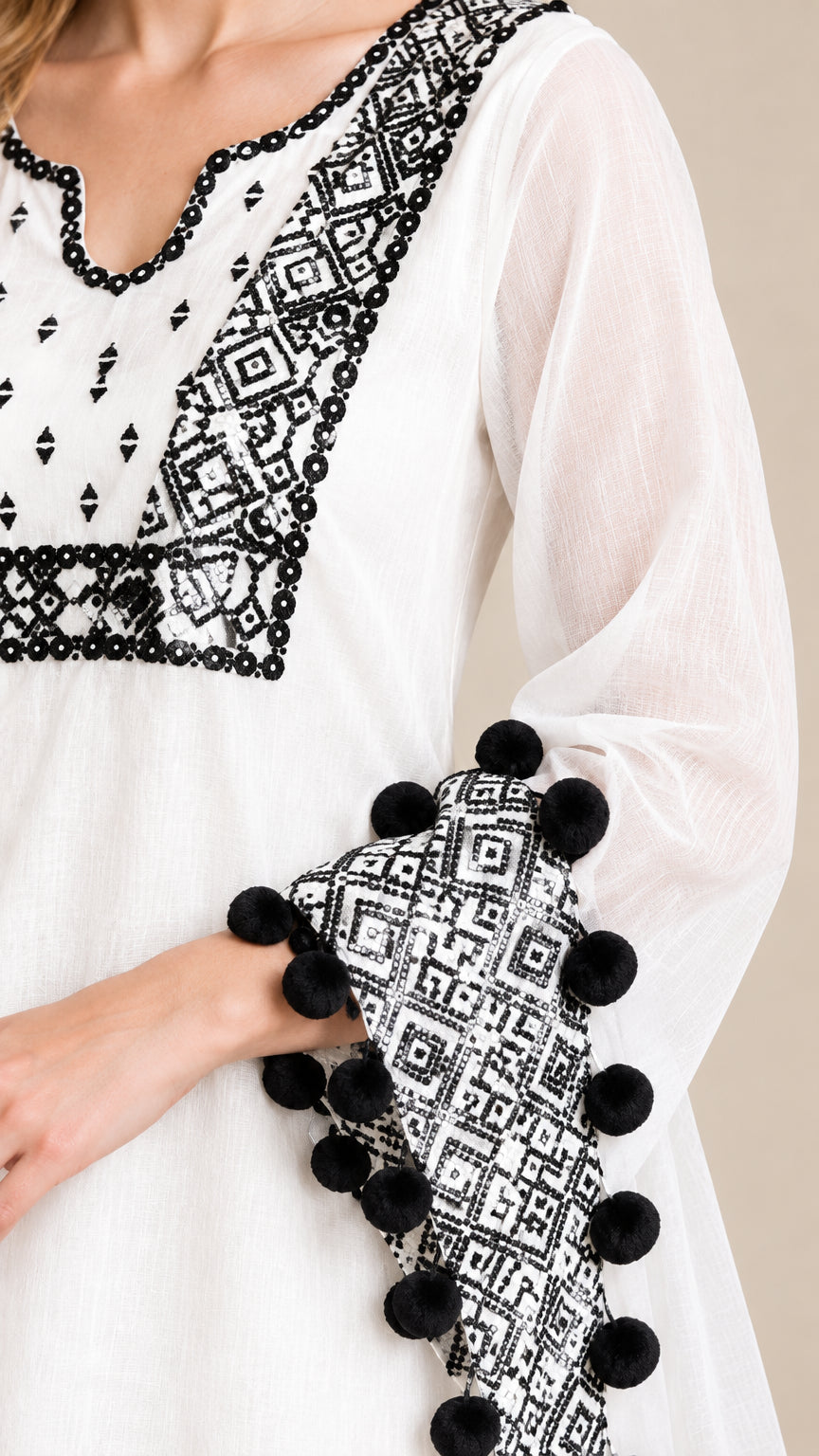 Close-up detail of geometric embroidery neckline and sleeve cuffs with pom-poms