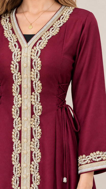 Close up of ornate gold embroidery and side tie detail on burgundy kaftan