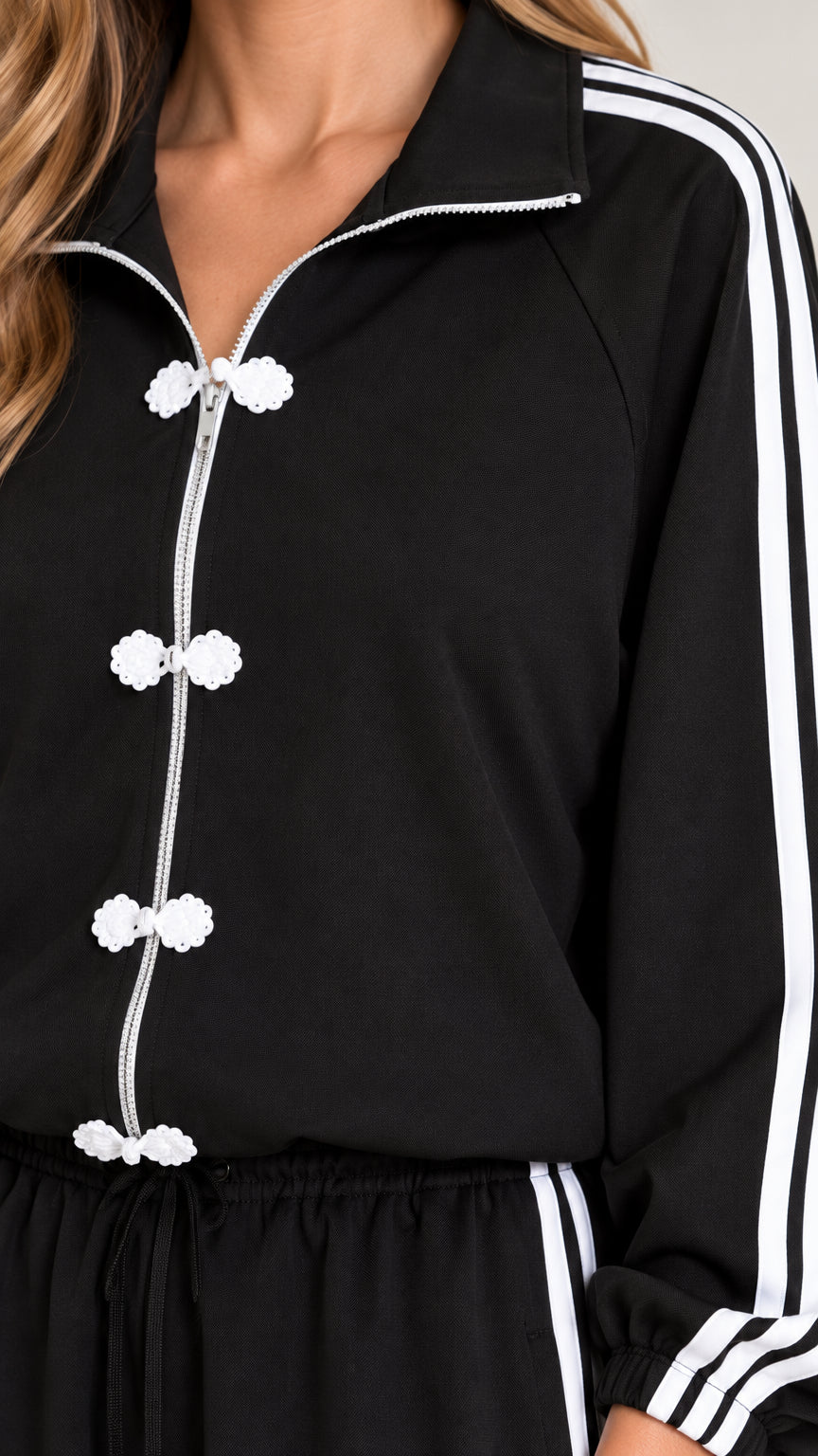 Close-up detail of zip front and white frog button closures on black tracksuit jacket