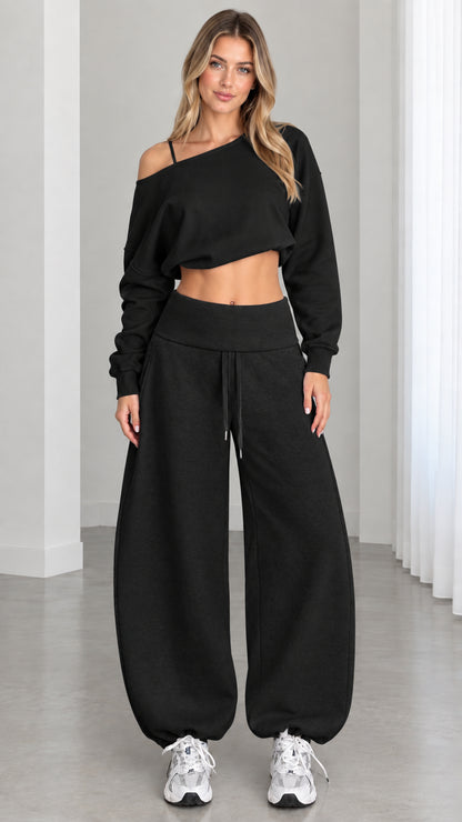 Model wearing all-black 2-piece off-the-shoulder cropped sweatshirt and balloon sweatpants set