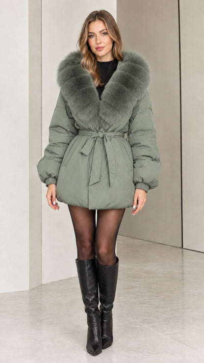 Front view of woman wearing sage green belted winter puffer coat with faux fur collar