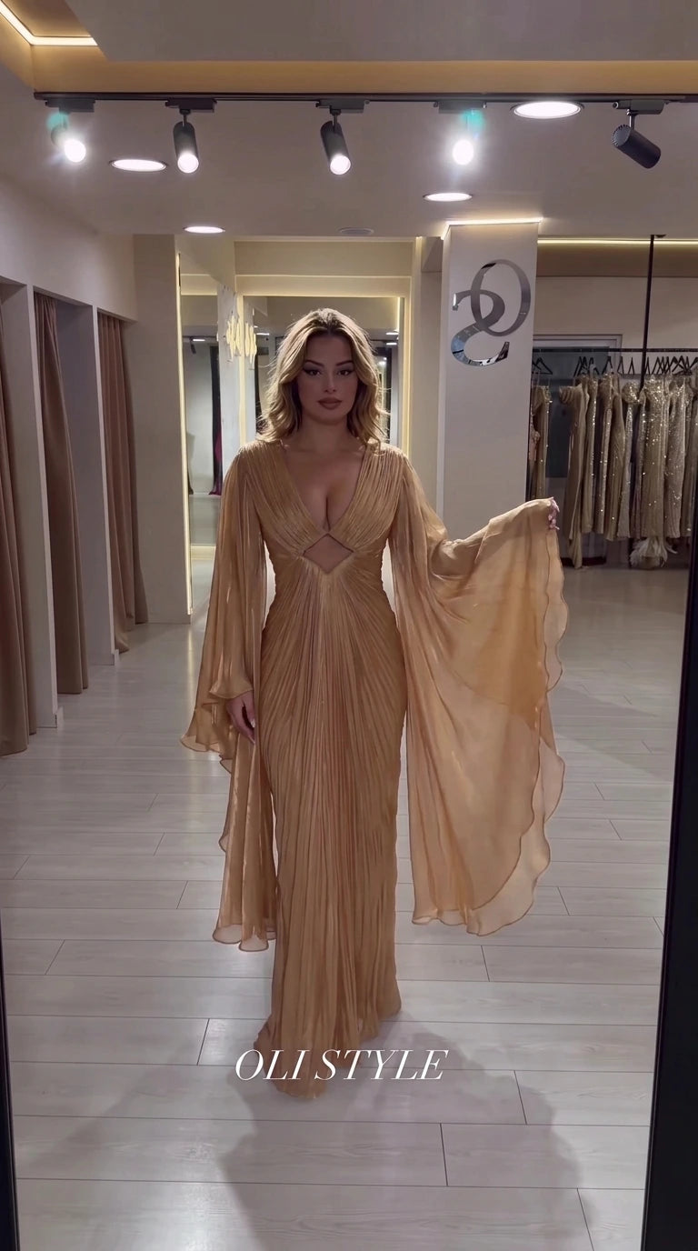 Champagne gold pleated floor-length gown with dramatic cape sleeves and waist cutout