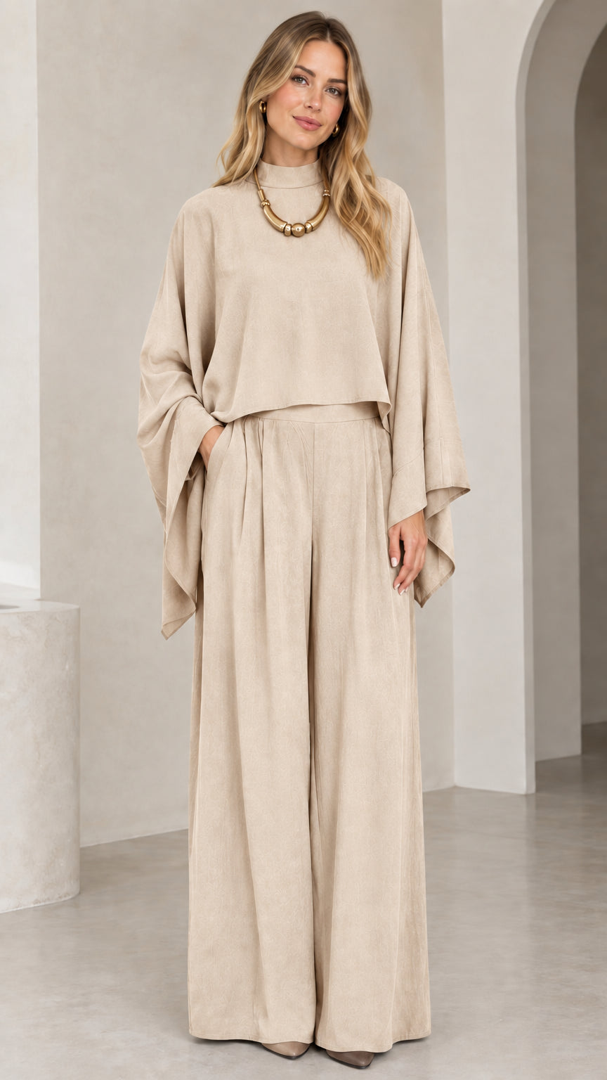 Full-length studio shot of woman in beige cream mock neck draped top and wide leg pants set